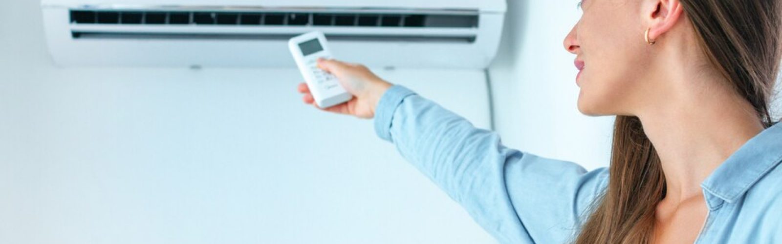 Woman using remote control to adjust ductless mini-split air conditioning unit, highlighting HVAC comfort solutions.
